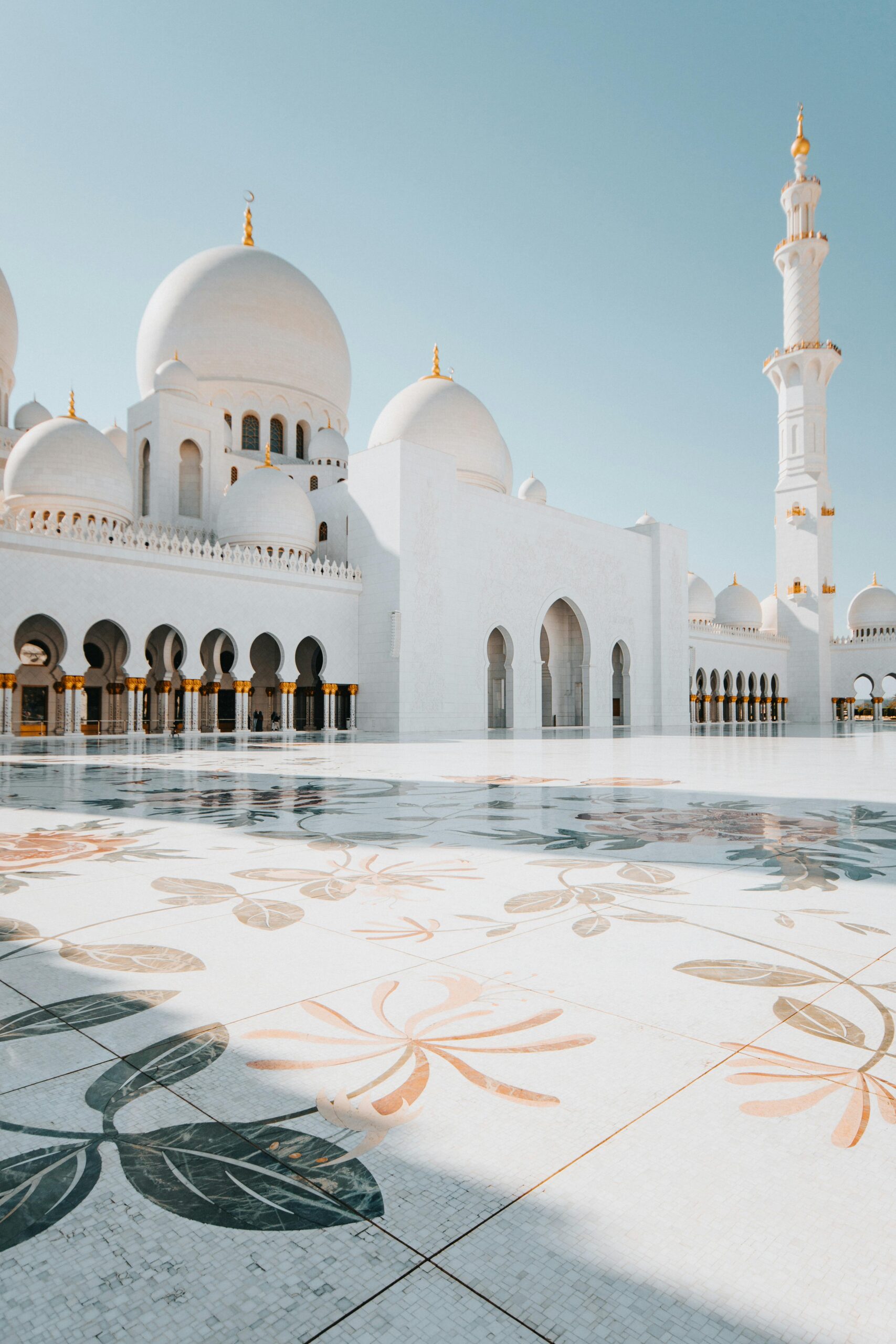 Stunning exterior view of Sheikh Zayed Grand Mosque with its iconic minaret and intricate flooring under clear blue sky.